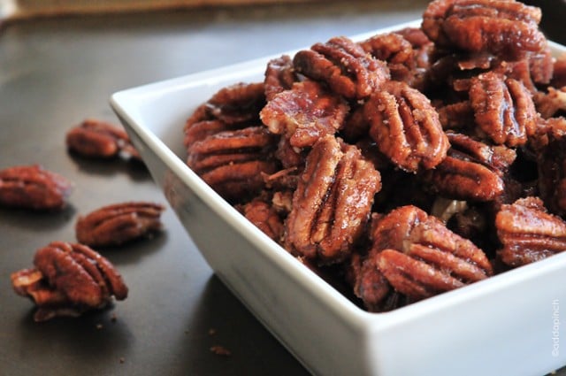 Cinnamon pecans in a white serving bowl on a dark surface.