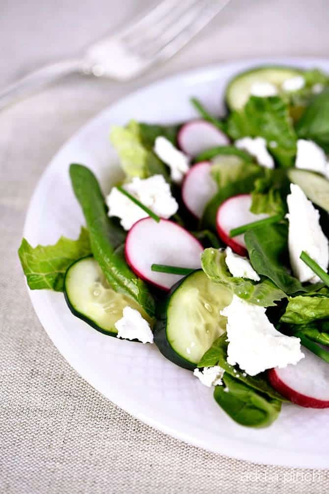 This Spinach Romaine Salad recipe makes a delicious welcome to spring! Topped with radishes, cucumbers, feta, and chives, it is sure to be a favorite! // addapinch.com