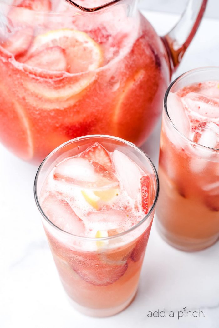 Glasses and a pitcher of strawberry lemonade with ice cubes and fresh strawberry and lemon slices. // addapinch.com