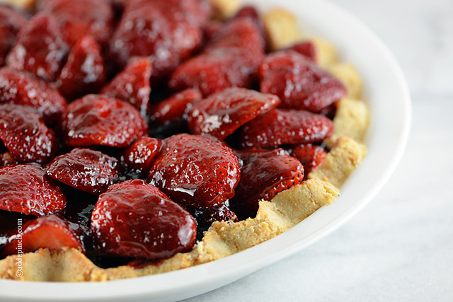 Strawberry Pie with homemade shortbread pie crust ina white pie dish on marble counter. ©addapinch.com
