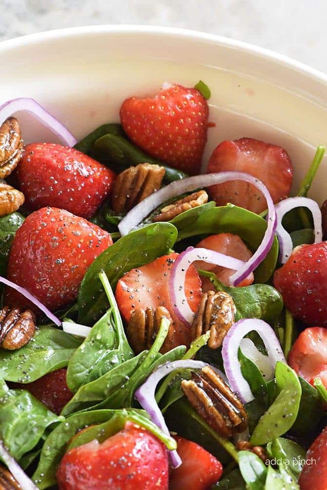 Photo of strawberry spinach salaad with spinach, strawberries, onion rings and pecans in white bowl.