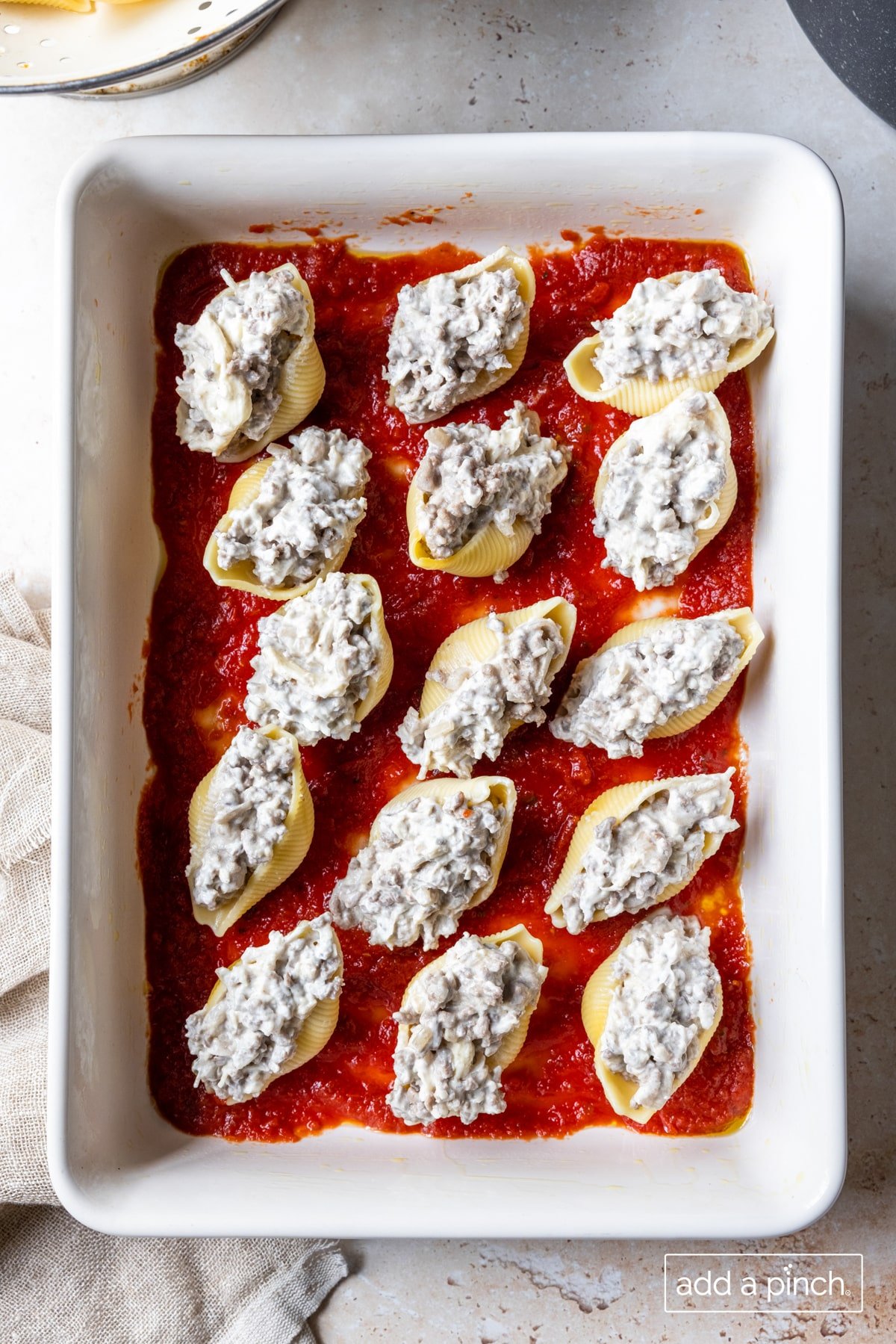 Photo of stuffed shells on tomato sauce in baking dish. 