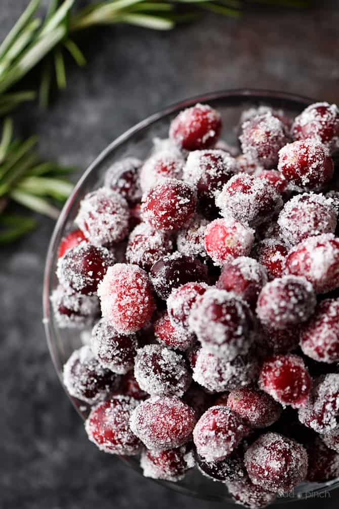 Sugared Cranberries in a serving bowl surrounded with rosemary garnish // addapinch.com