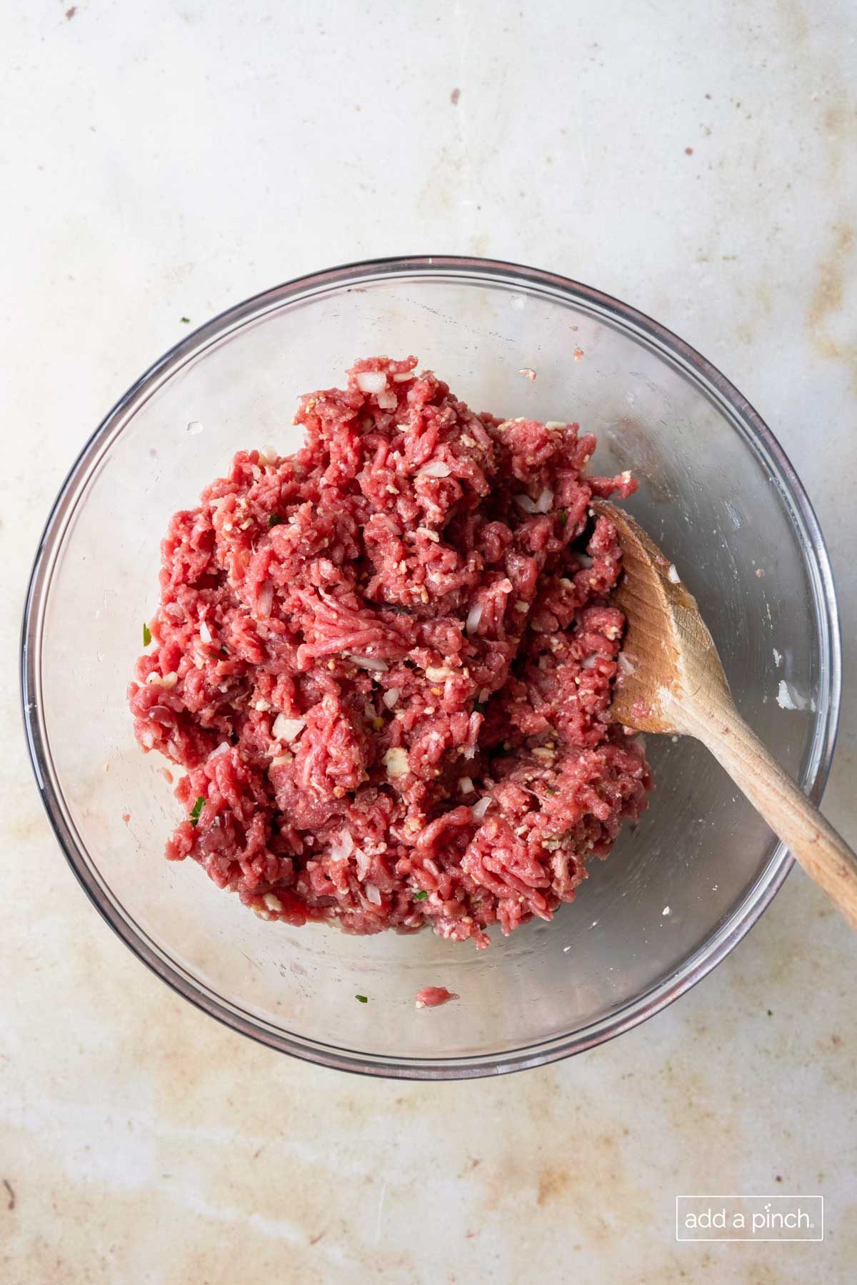 Meatball mixture is blended in a glass mixing bowl.