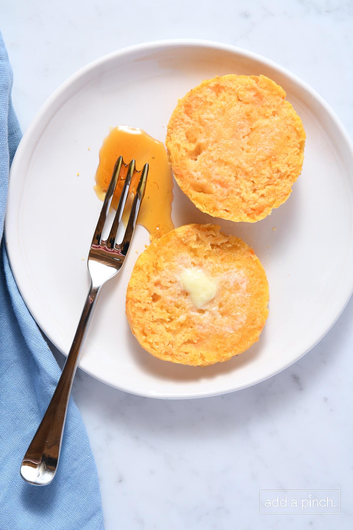 Sweet potato biscuit opened on a white plate with butter on top and honey and a fork to the side.