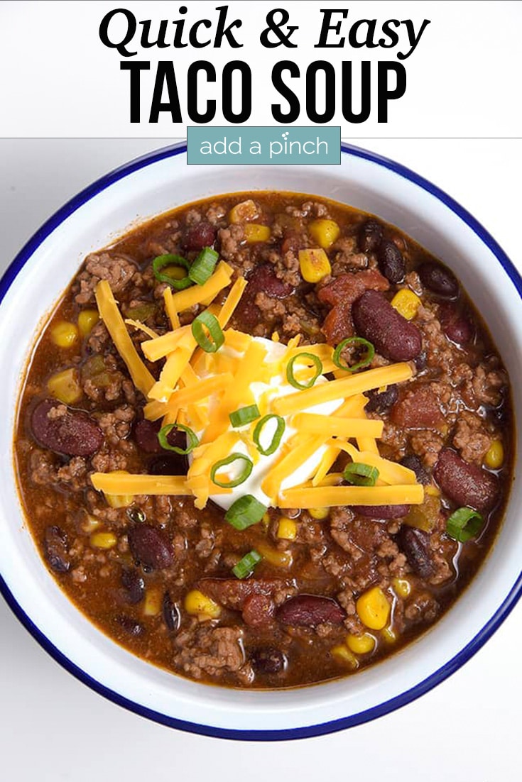 Taco Soup garnished with shredded cheese, sour cream and onion, served in a white bowl with blue rim.