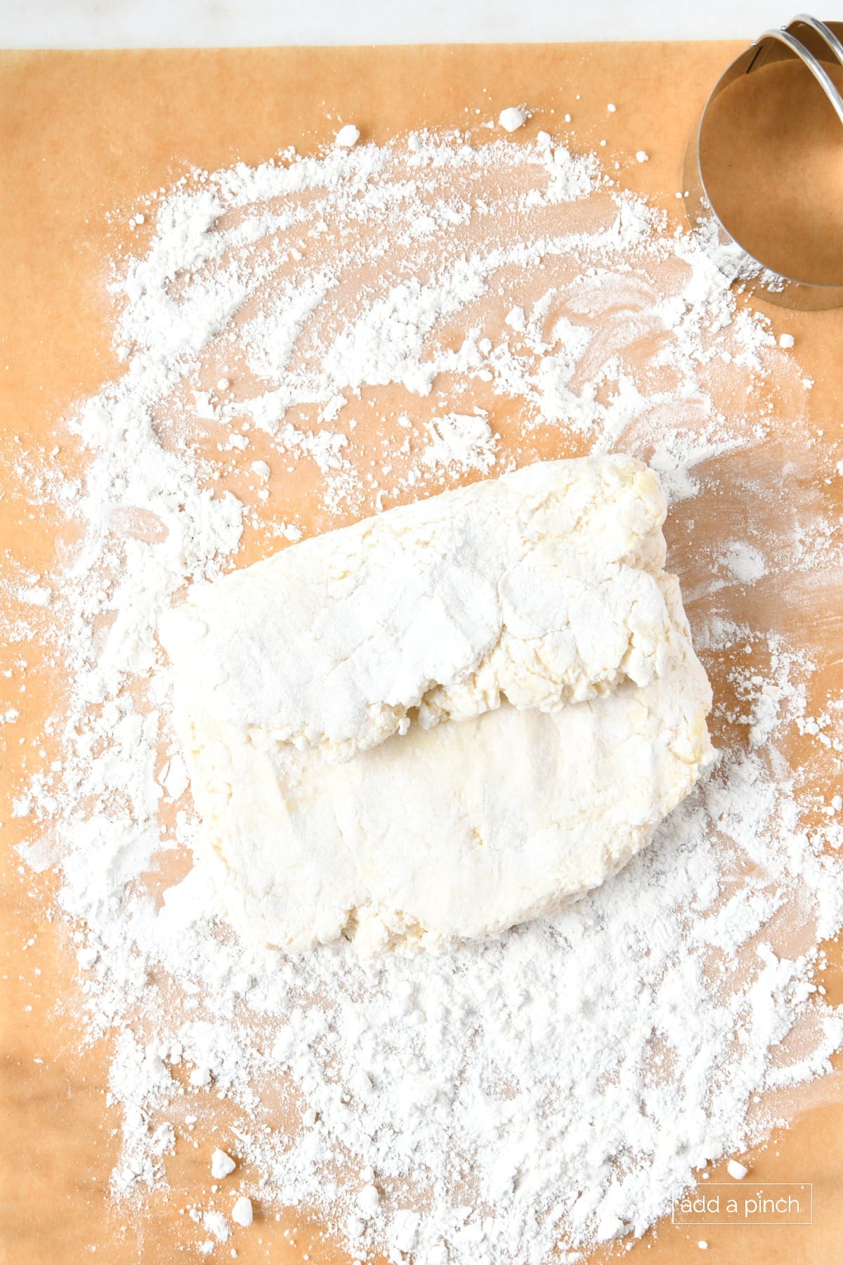 Patting and folding biscuit dough into more layers on a floured surface.