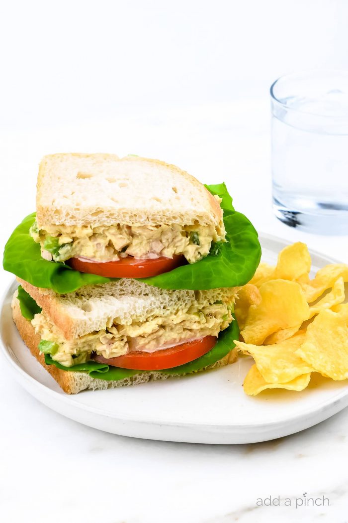 White plate with tuna salad sandwich sliced and stacked, with chips and water // addapinch.com