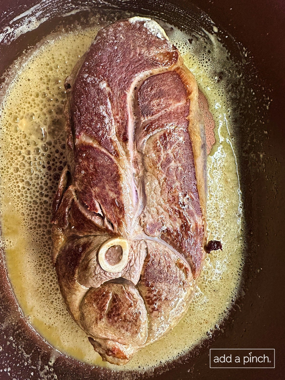 Venison roast (deer roast) searing in pan with butter and olive oil.
