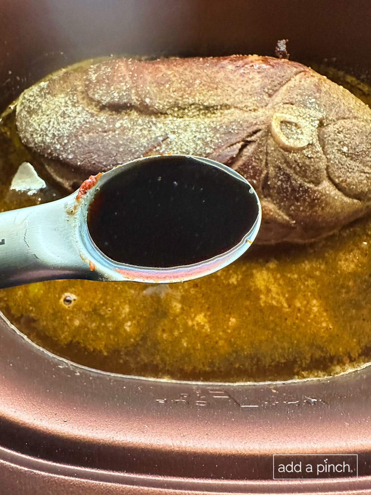 Coconut aminos in measuring spoon being added to slow cooker.