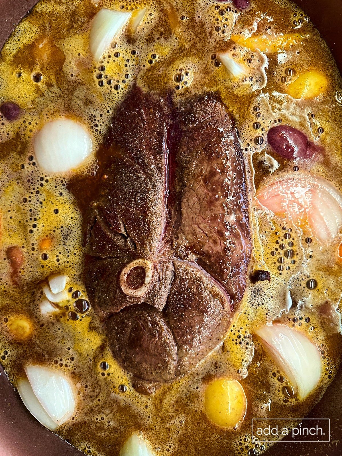 Deer roast cooking in slow cooker with vegetables and liquids for stew.