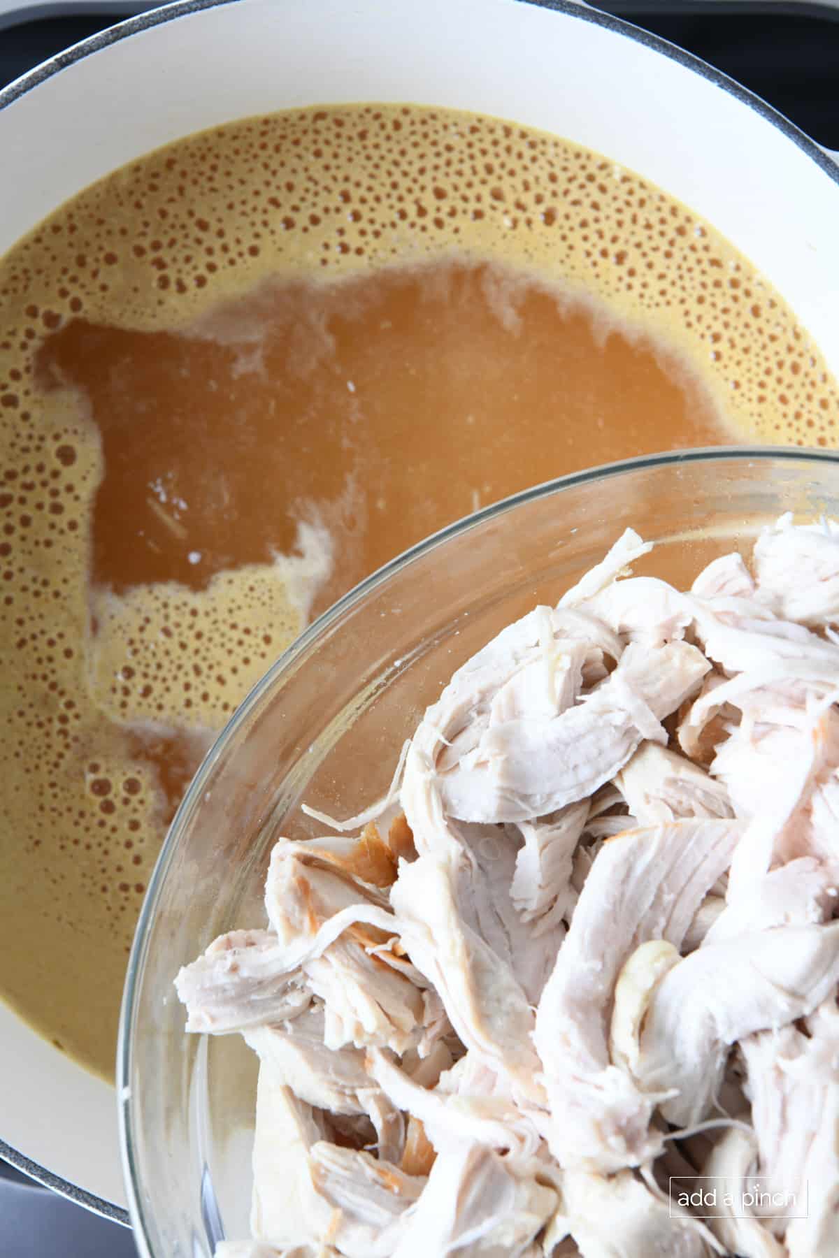 Shredded chicken added back to chicken stock in a white Dutch oven.