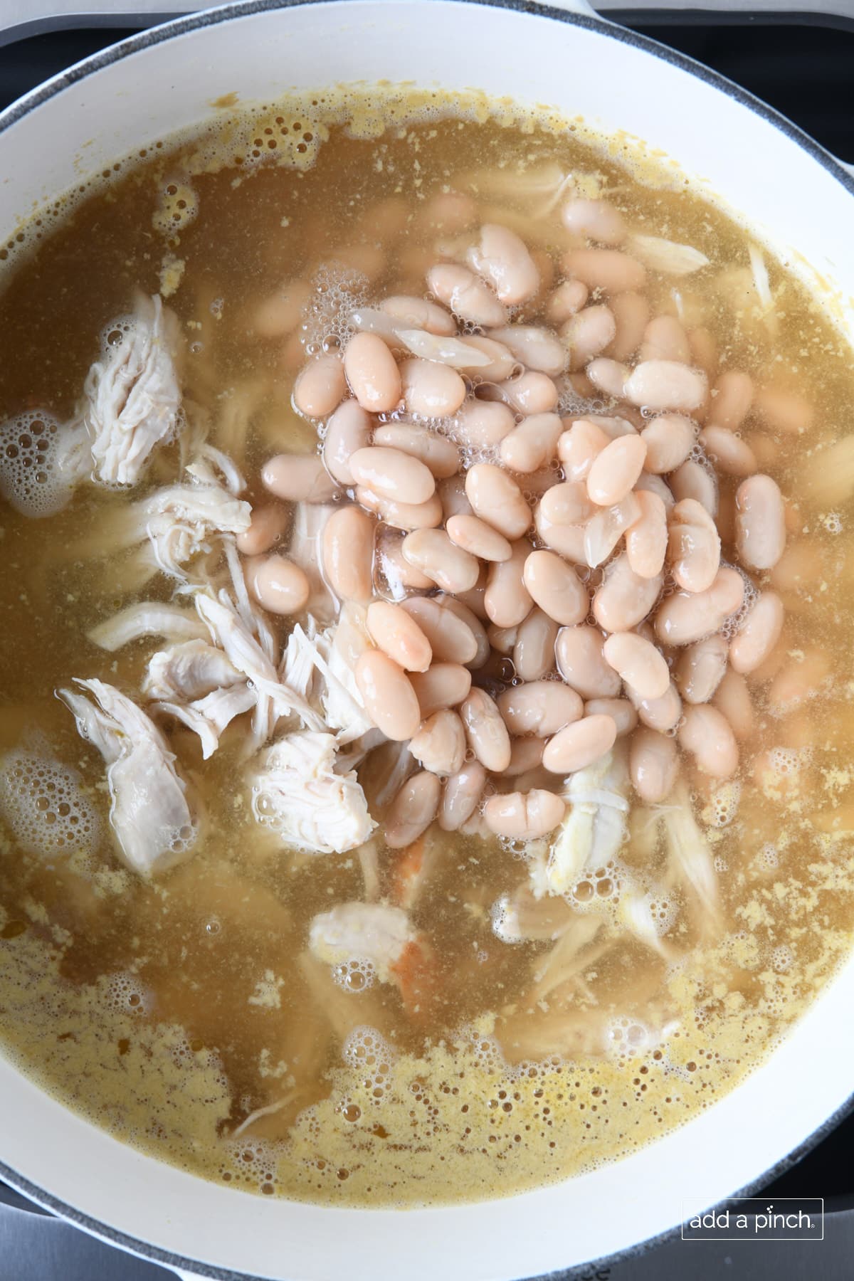 White beans, shredded chicken, and chicken stock in a white Dutch oven.