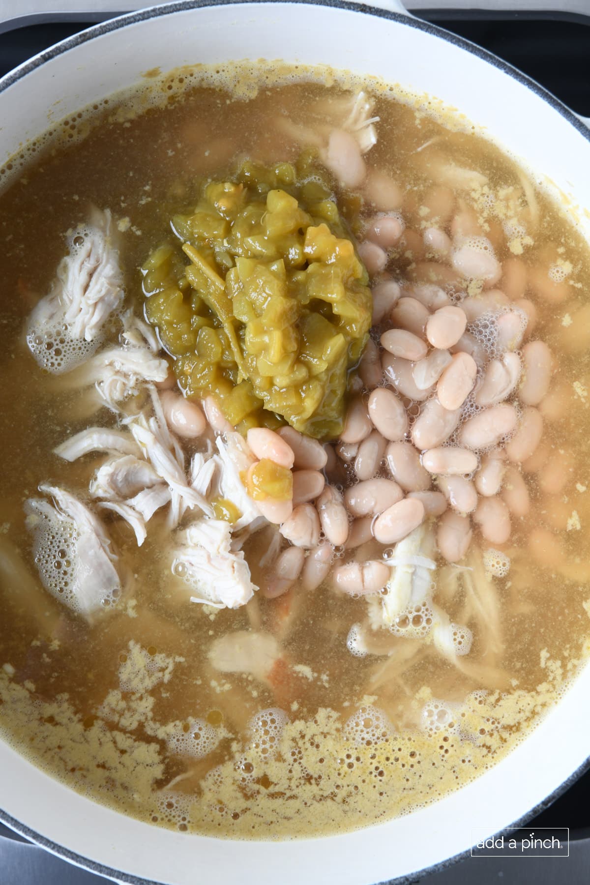 Green chilis, white beans, shredded chicken breast, and chicken stock in a white Dutch oven.