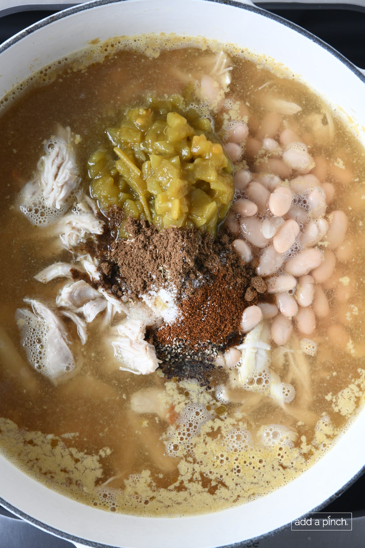 Seasonings added to White Chicken Chili in a white Dutch oven.