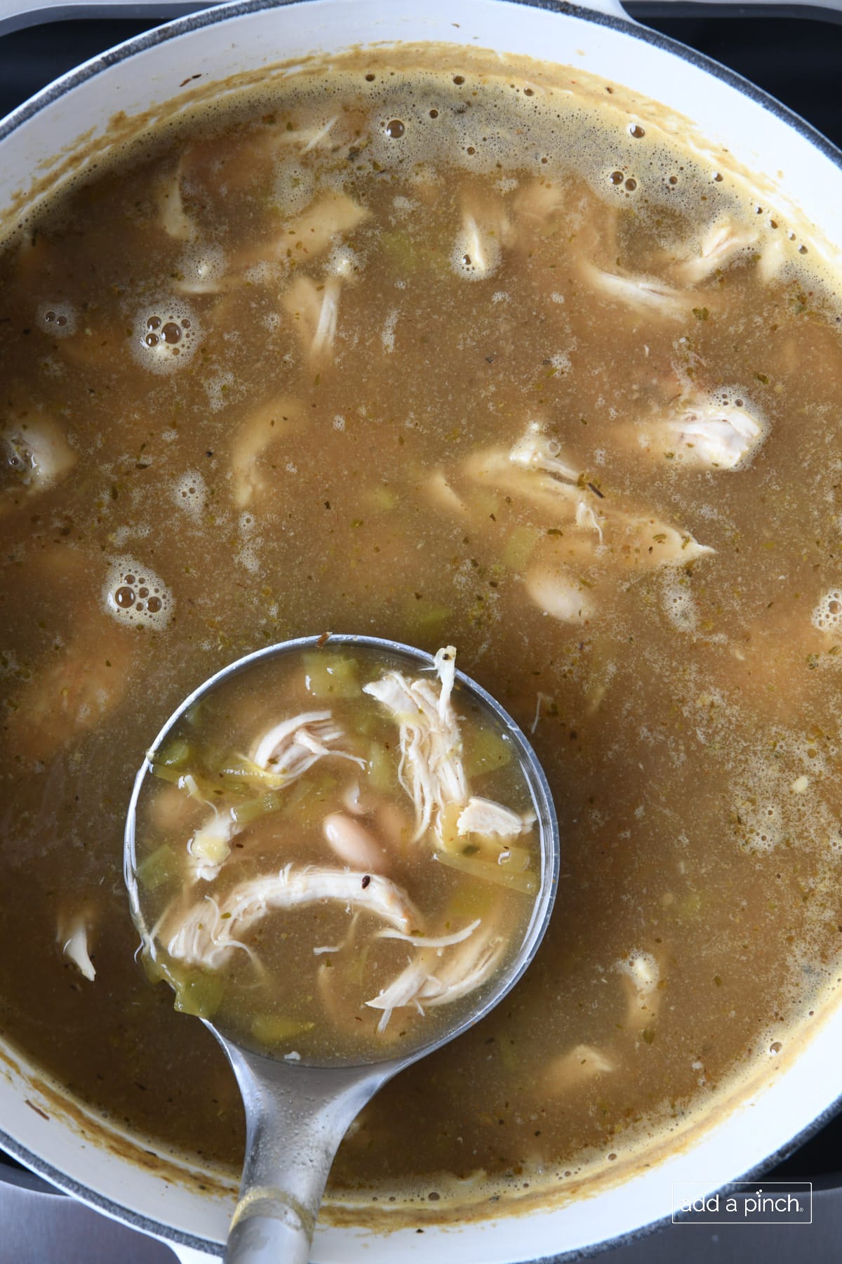 A ladle of white chicken chili in a white dutch oven.